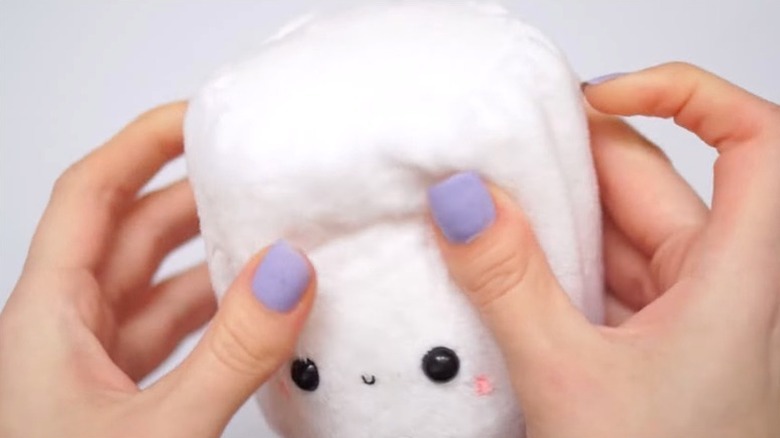 Woman's hands squeezing a DIY white plushie with smiling face