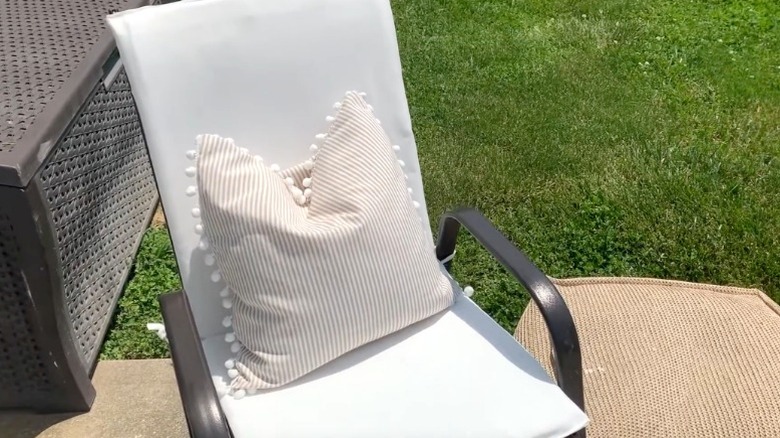 Metal patio chair with white DIY cushions and a striped pillow on a patio near lawn