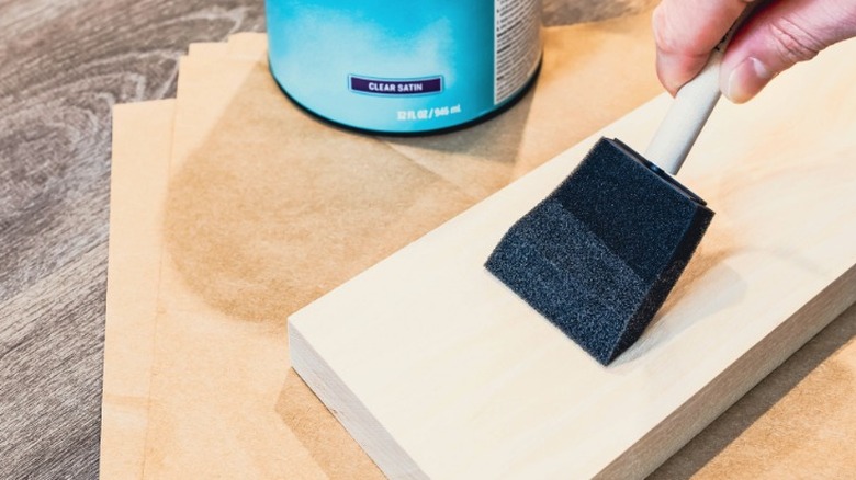 Person applying clear satin stain to wood board with a sponge brush