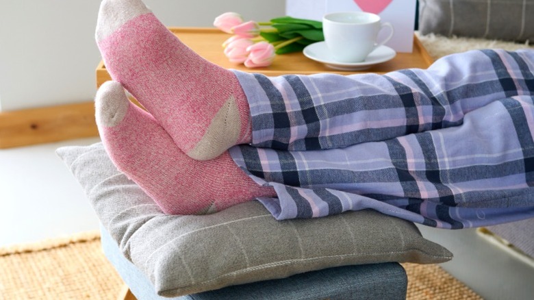 Person in pink socks and plaid pajamas resting feet on foot stool