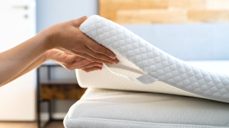 person lifting mattress topper corner off mattress