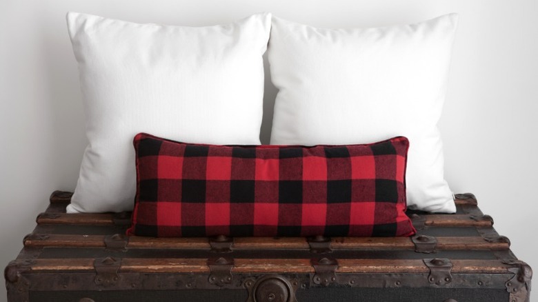 Red buffalo plaid lumbar pillow with two square white pillows on a wooden chest