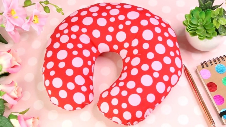 Red neck pillow with white polka dots on table next to a plant and a notebook