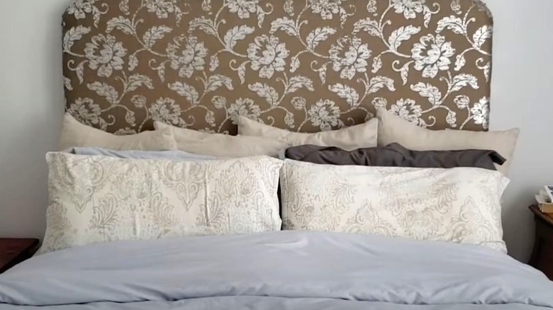 DIY padded headboard with floral patterned fabric behind a made bed