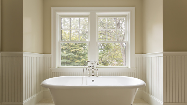 Bathroom with large uncovered windows behind a claw foot tub