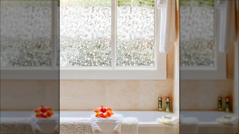 Bathroom with a tub below a window with decorative privacy film on it