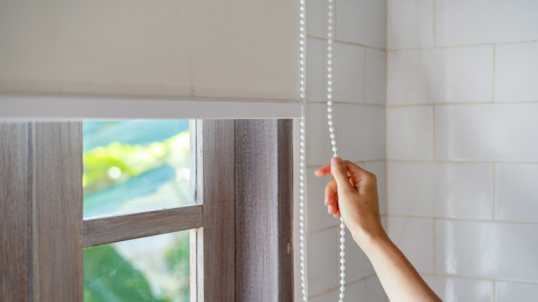 Woman pulling the cord on roller shades in a bathroom window