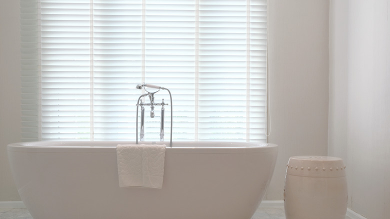 White bathtub in front of Venetian blinds that are drawn closed