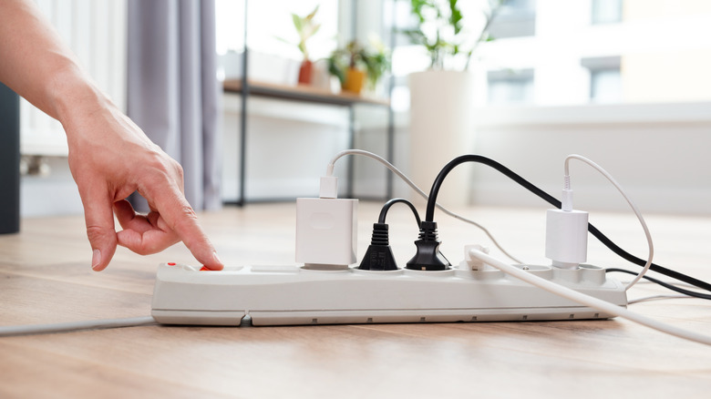 A hand turning on a power strip containing several plugs