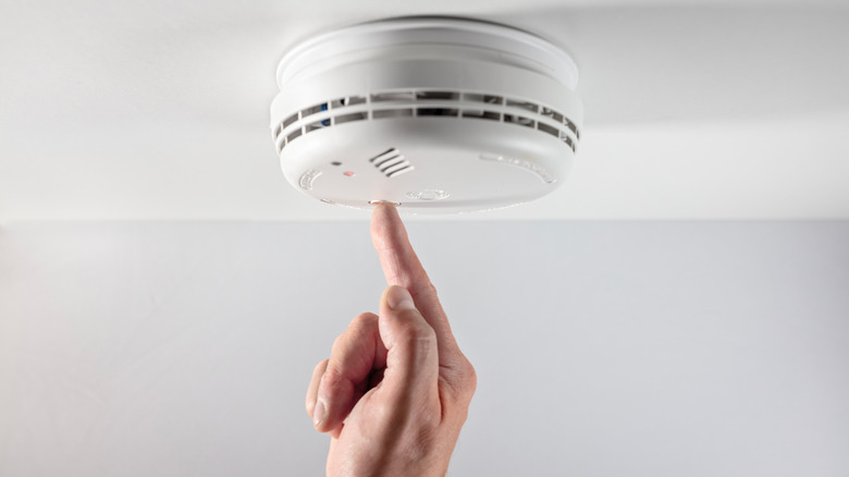 A person inspecting a smoke alarm by pushing the test button