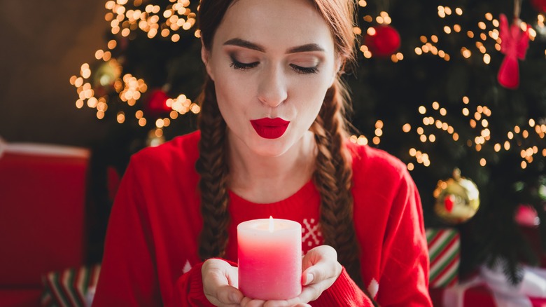 A person blowing out a red candle against Christmas tree background