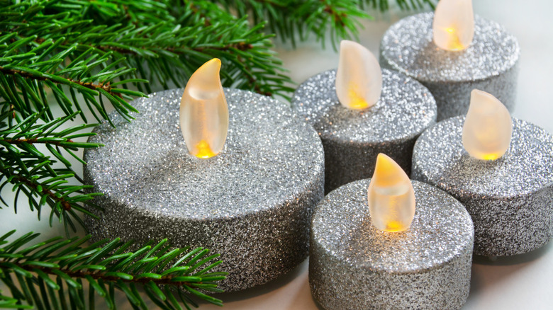 Glittery silver LED candles near conifer branches