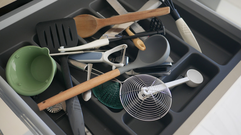 Kitchen utensils are strewn inside a cluttered drawer