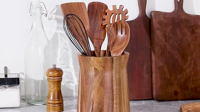 A kitchen utensil holder made of acacia wood sits next to a jar