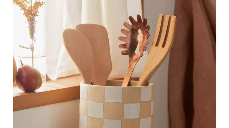 A checkerboard crock full of wooden kitchen utensils sits on a pile of cookbooks