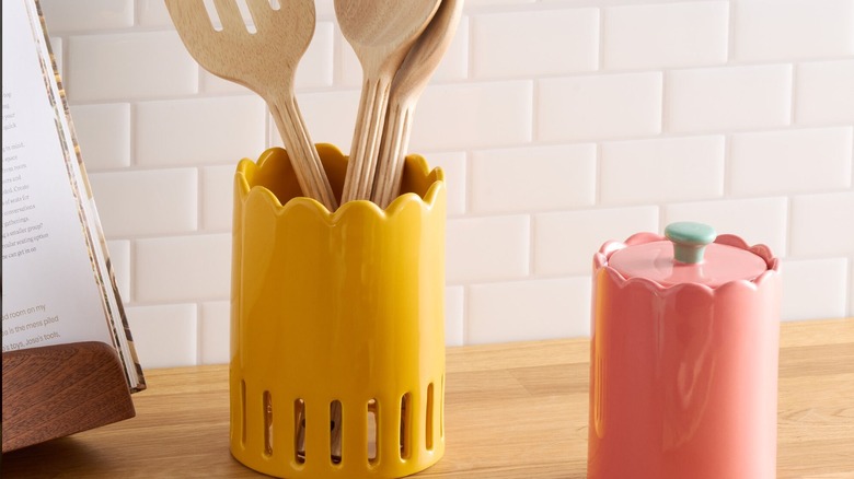 Wooden kitchen utensils sit in a bright yellow holder next to an open cookbook