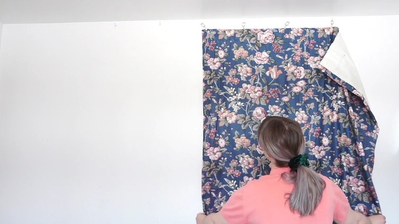 Woman hanging floral curtains on white wall