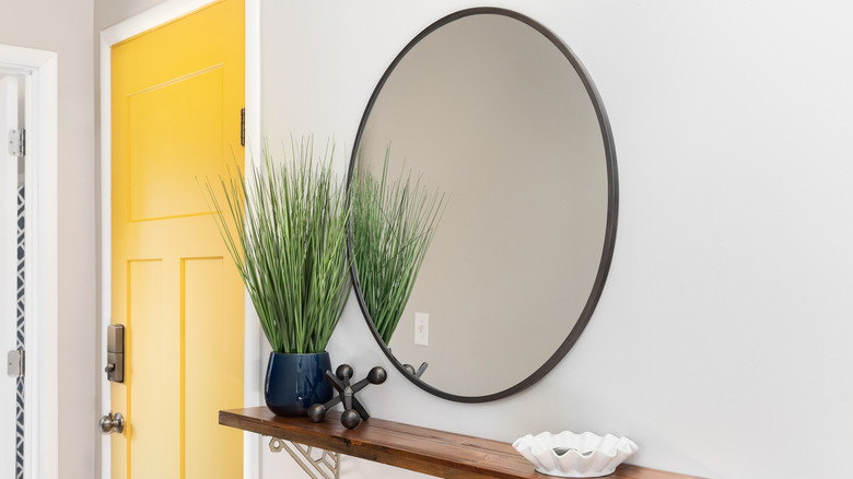 Round mirror above wooden shelf next to yellow door