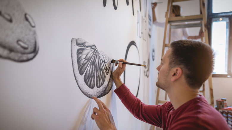 Man painting black and white orange slice on wall