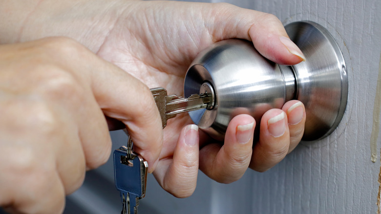 Hands unlocking a chrome doorknob lock with a square key.