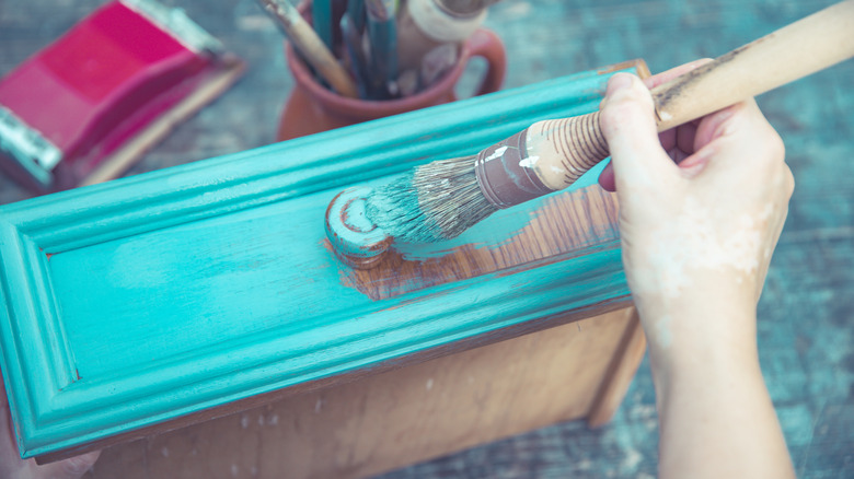 A hand painting a drawer with teal chalk paint.