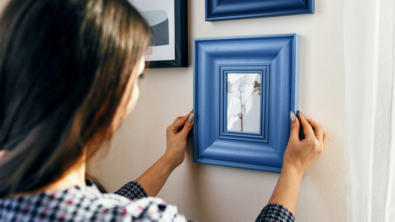 A woman hanging a blue picture frame up in a gallery wall configuration.