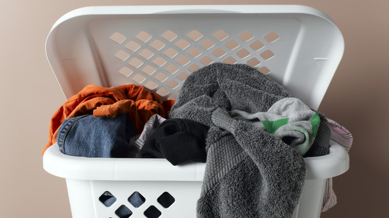 A white plastic laundry hamper fill with dirty clothes and towels.