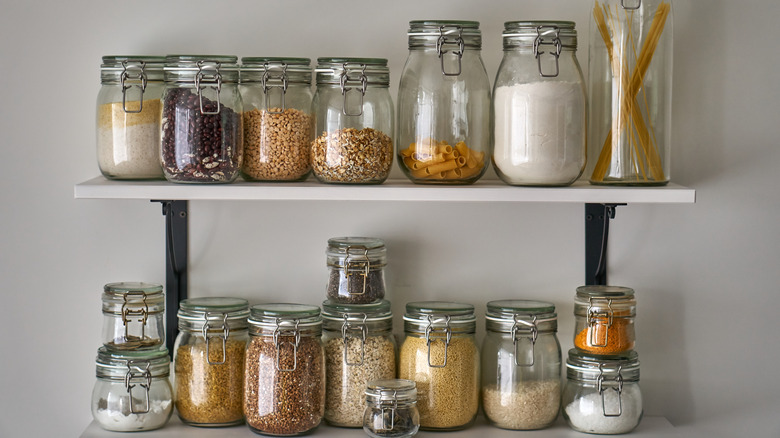 Jars filled with dry goods lined up on two shelves on the wall.