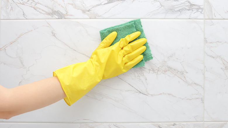 A gloved hand wiping down a marble tiled wall.