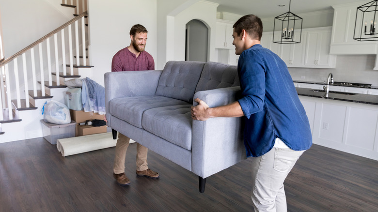 Two men lifting a gray love seat.