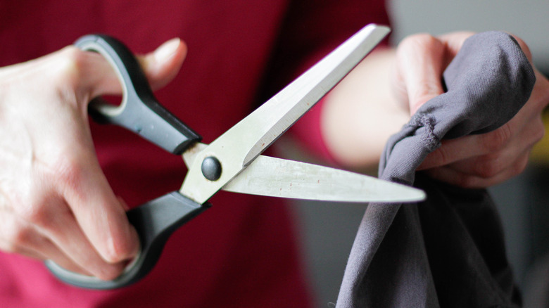 Hands holding scissors about to cut through dark fabric.