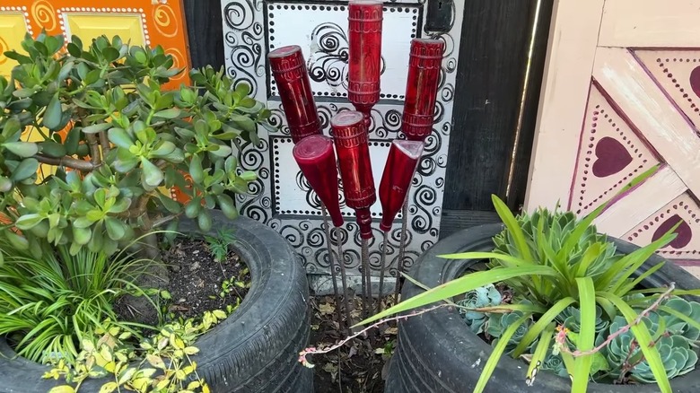 A red glass bottle tree between two tires containing plants