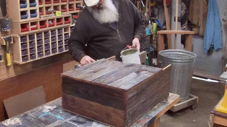 A man crafting and staining a bathroom cabinet made from old fence posts.