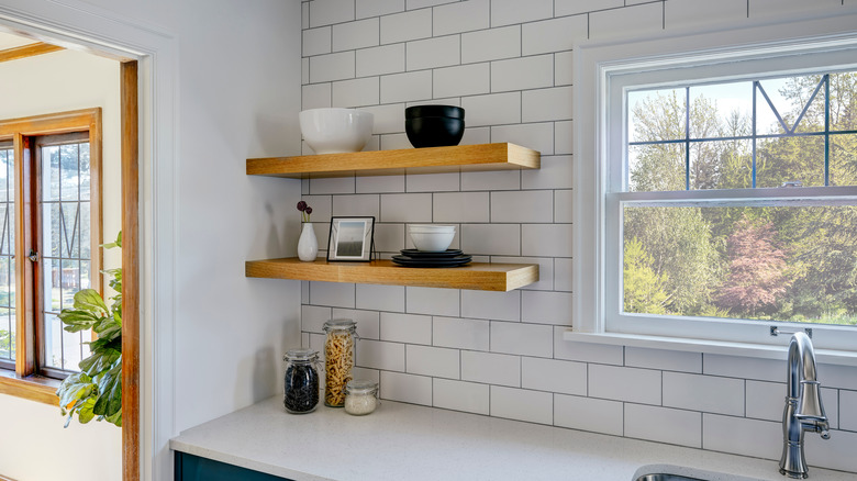 Floating wooden wall shelves in kitchen against white tile