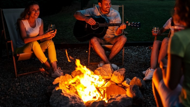 Friends gathered around a firepit while someone plays guitar