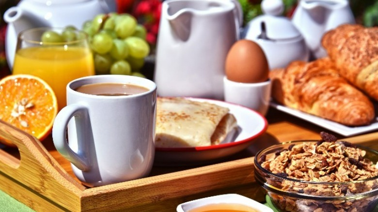 A large wood tray carrying brunch foods and coffee