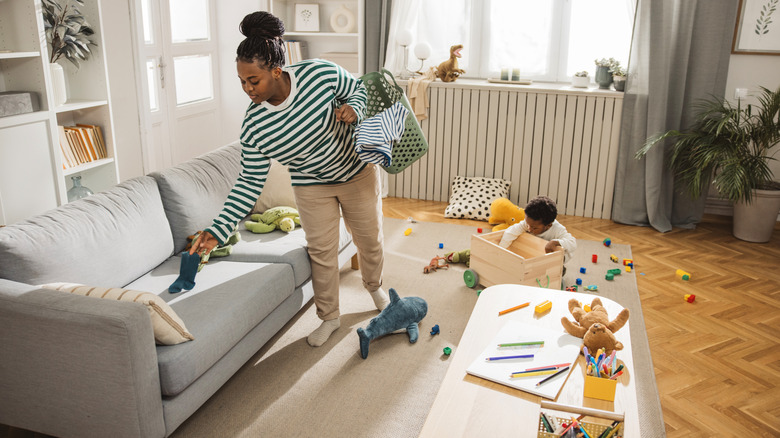 A mother cleans up a living room full of toys