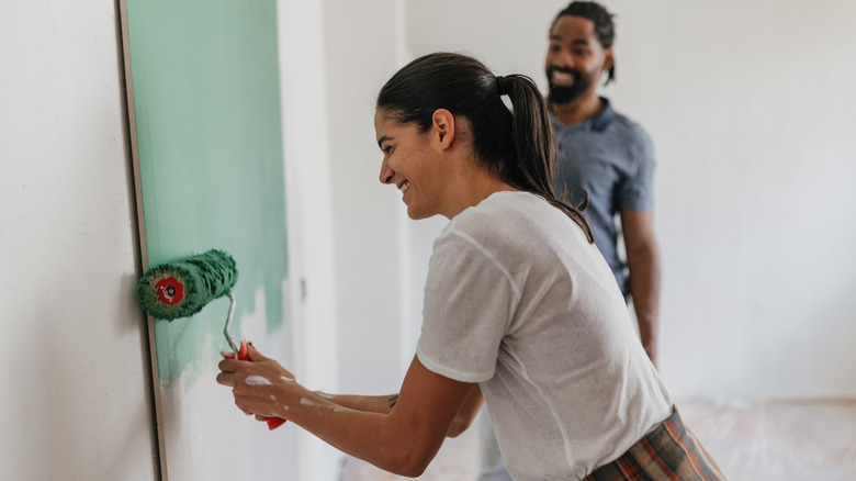 A couple smiling and painting their walls green