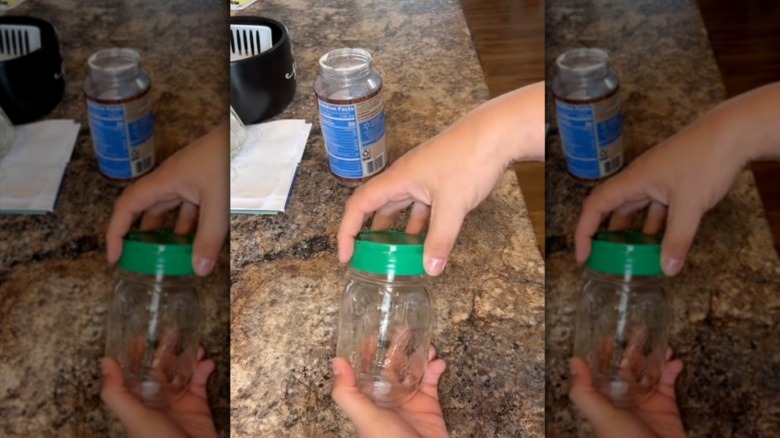 A hand screws the lid from a parmesan cheese container onto a mason jar.