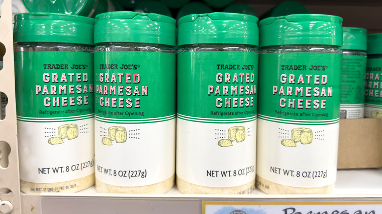 A row of Trader Joe's grated parmesan cheese containers for sale on the shelf in a store.