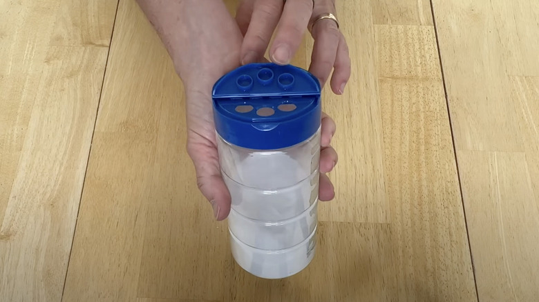 Two hands hold a parmesan cheese container filled with baking soda.