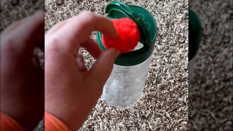 Hand placing a pom pom in an empty parmesan container.