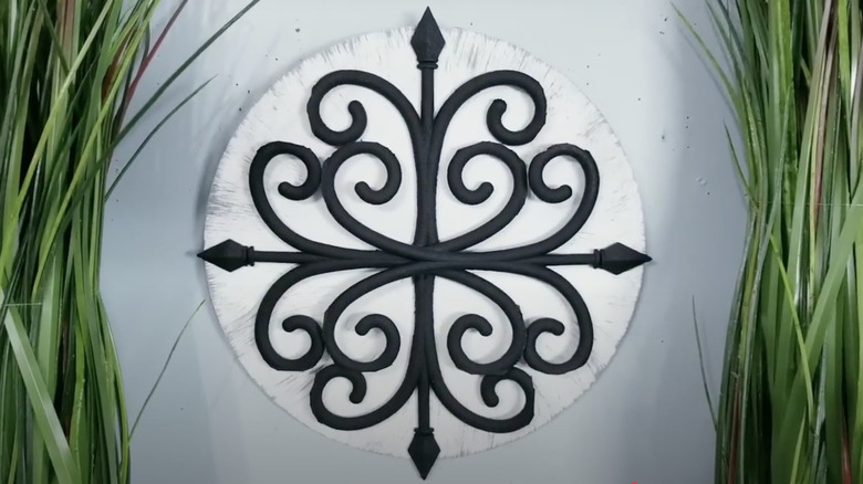 A wrought iron look wall medallion made from Dollar Tree garden fence and a wooden disc