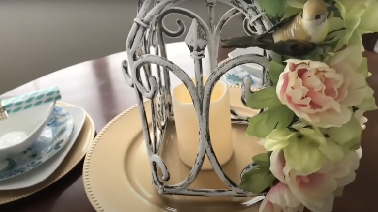 A faux birdcage table centerpiece made using Dollar Tree garden fence and artificial flora and fauna