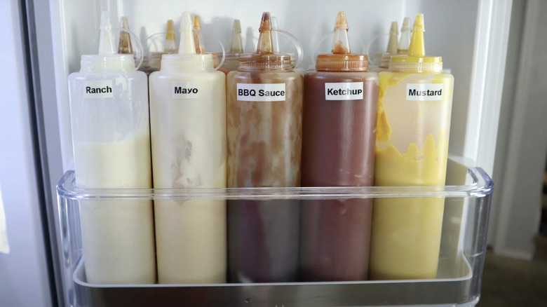 Labeled condiment bottles filled with sauces and stored in the fridge door.