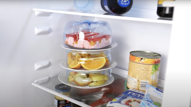 A stacked storage unit for the fridge made from ceramic dinner plates and a used plastic water jug.