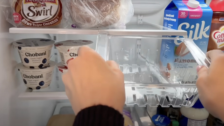 A person attaches a clip-on basket from Dollar Tree to a fridge shelf.