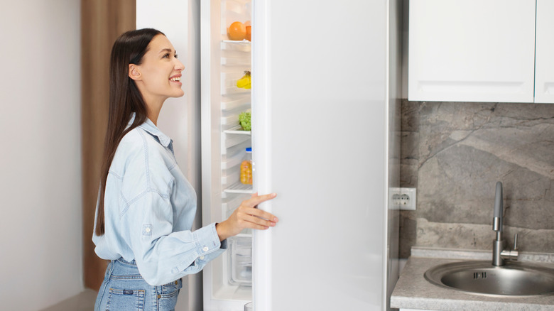 A woman looks at the open door of her fridge with a smile on her face.