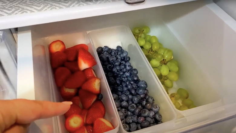 Grapes and berries stored in trays in a fridge drawer.