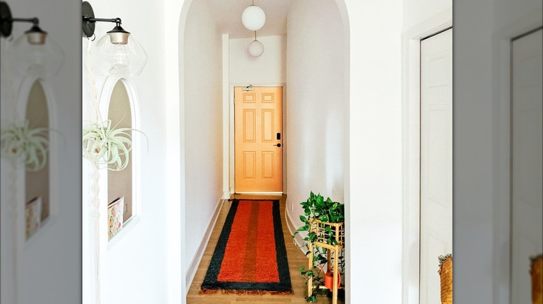 A white entryway with wooden front door and red and black rug